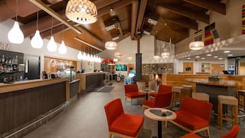 Un moderno hall de hotel con área de bar, asientos rojos y lámparas colgantes.