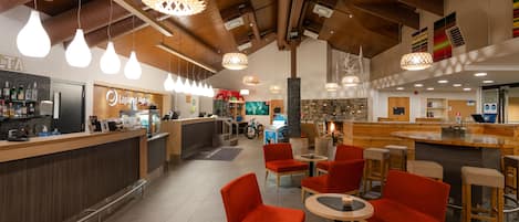 Un moderno hall de hotel con área de bar, asientos rojos y lámparas colgantes.