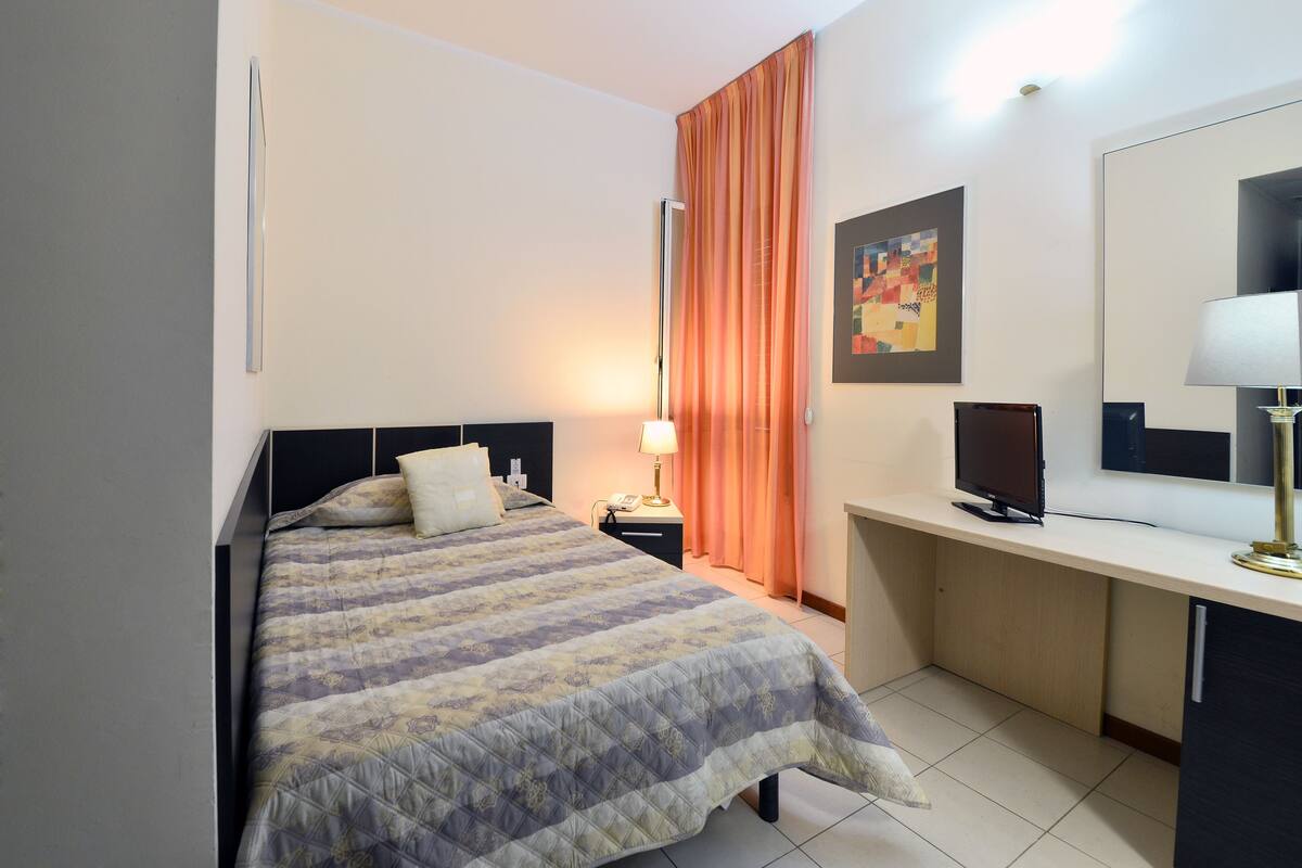 A hotel room with a bed, a desk, a television, a lamp, and a painting on the wall.