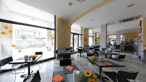 A spacious dining area with large windows, tables with orange napkins, and sunflowers. - Hotel Ferrari (Chiavari)