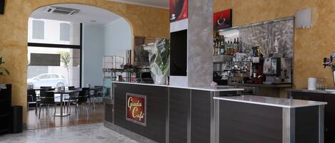 Interior moderno de una cafetería con suelo de mármol, una barra con el letrero 'Giada Cafe' y una zona de bar con diversas bebidas y una máquina de café.