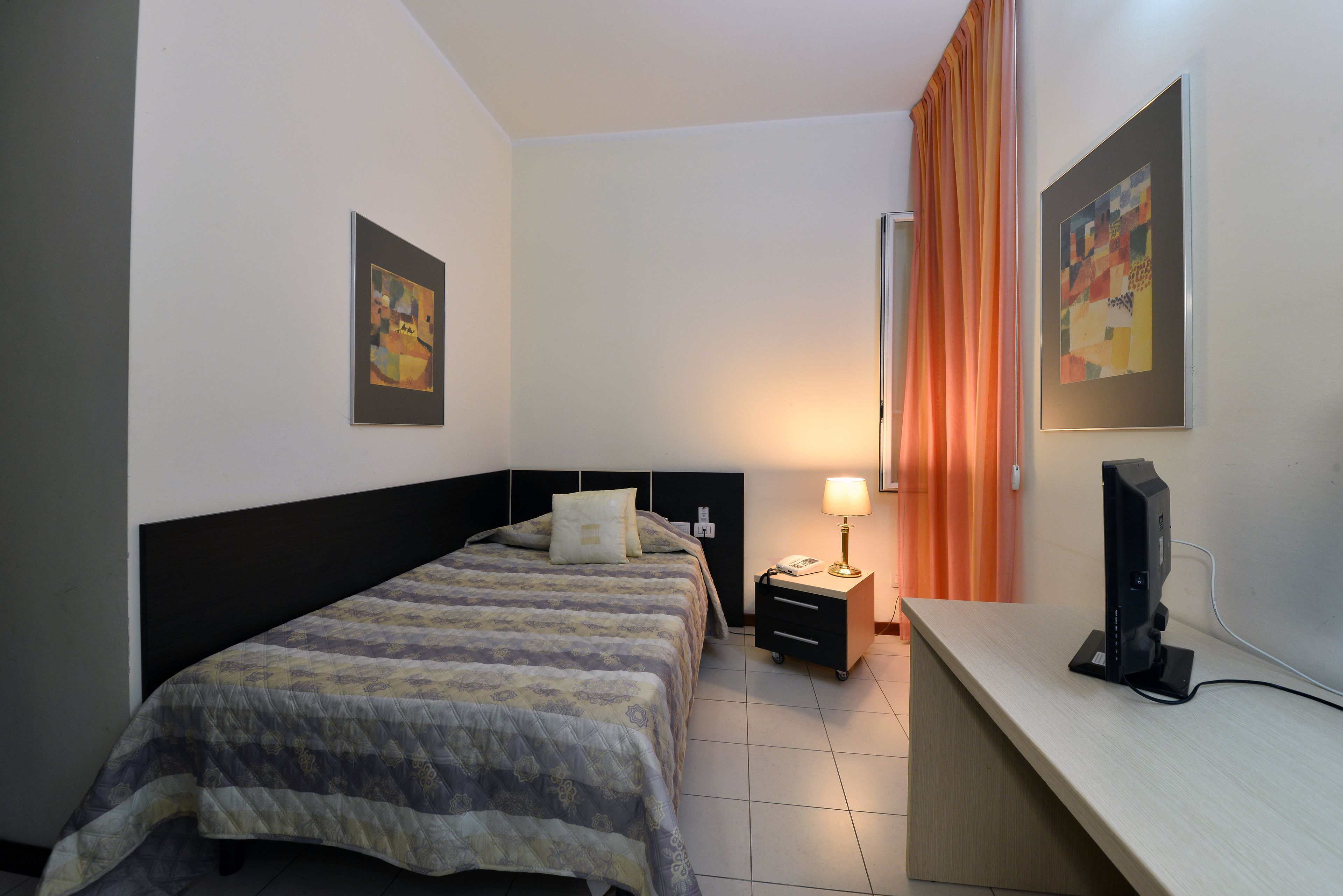 Una habitación de hotel con cama, escritorio, lámpara y televisión.