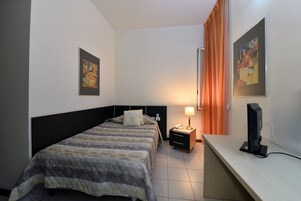 Una habitación de hotel con cama, escritorio, lámpara y televisión.