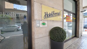 A hotel entrance with a sign reading "Hotel Ferrari," a large potted plant, and a visible parking area. - Hotel Ferrari (Chiavari)