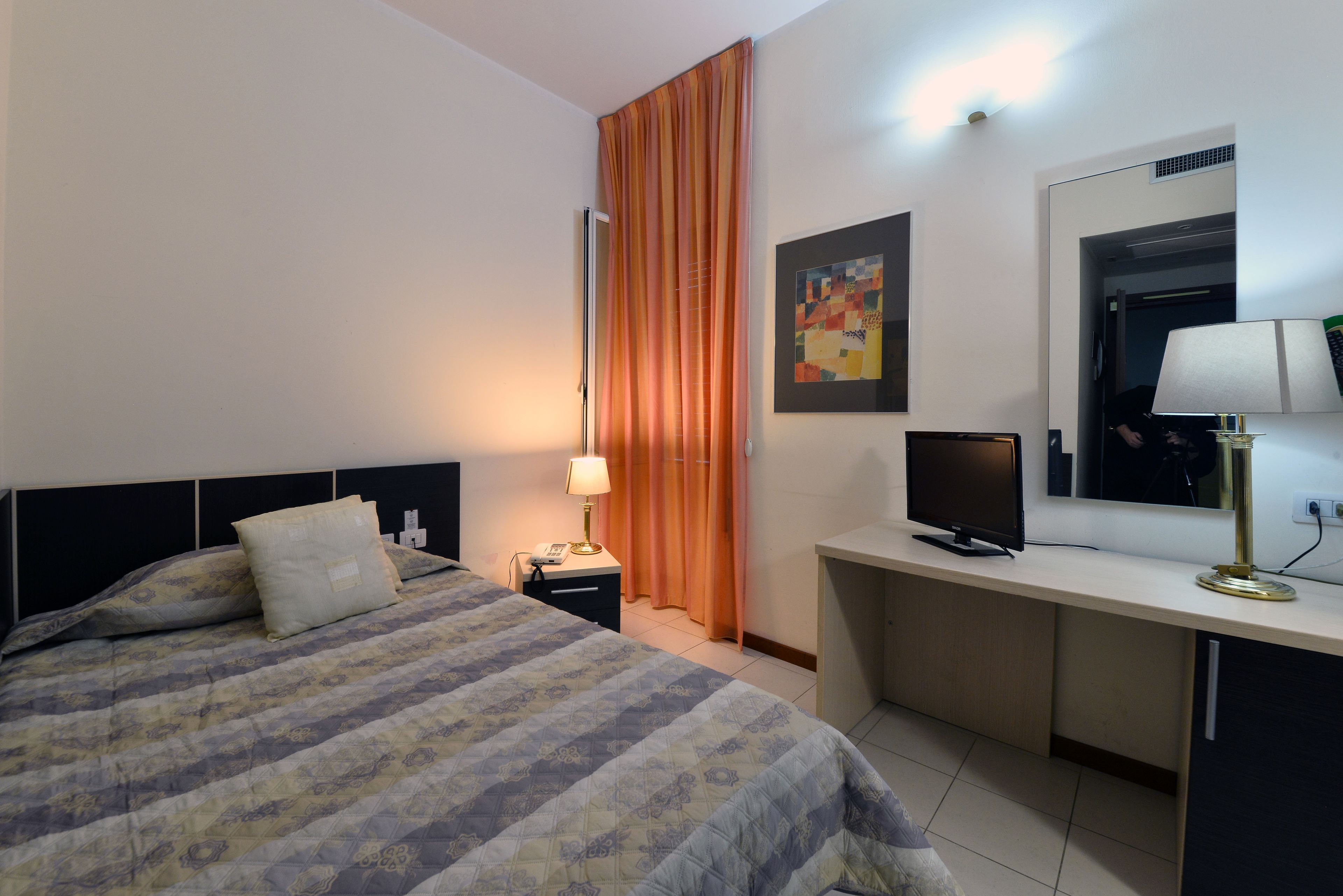 A hotel room with a bed, desk, lamp, television, and curtains.