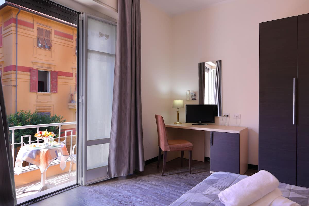 A hotel room with a balcony, a desk with a chair, a bed, and a wardrobe.