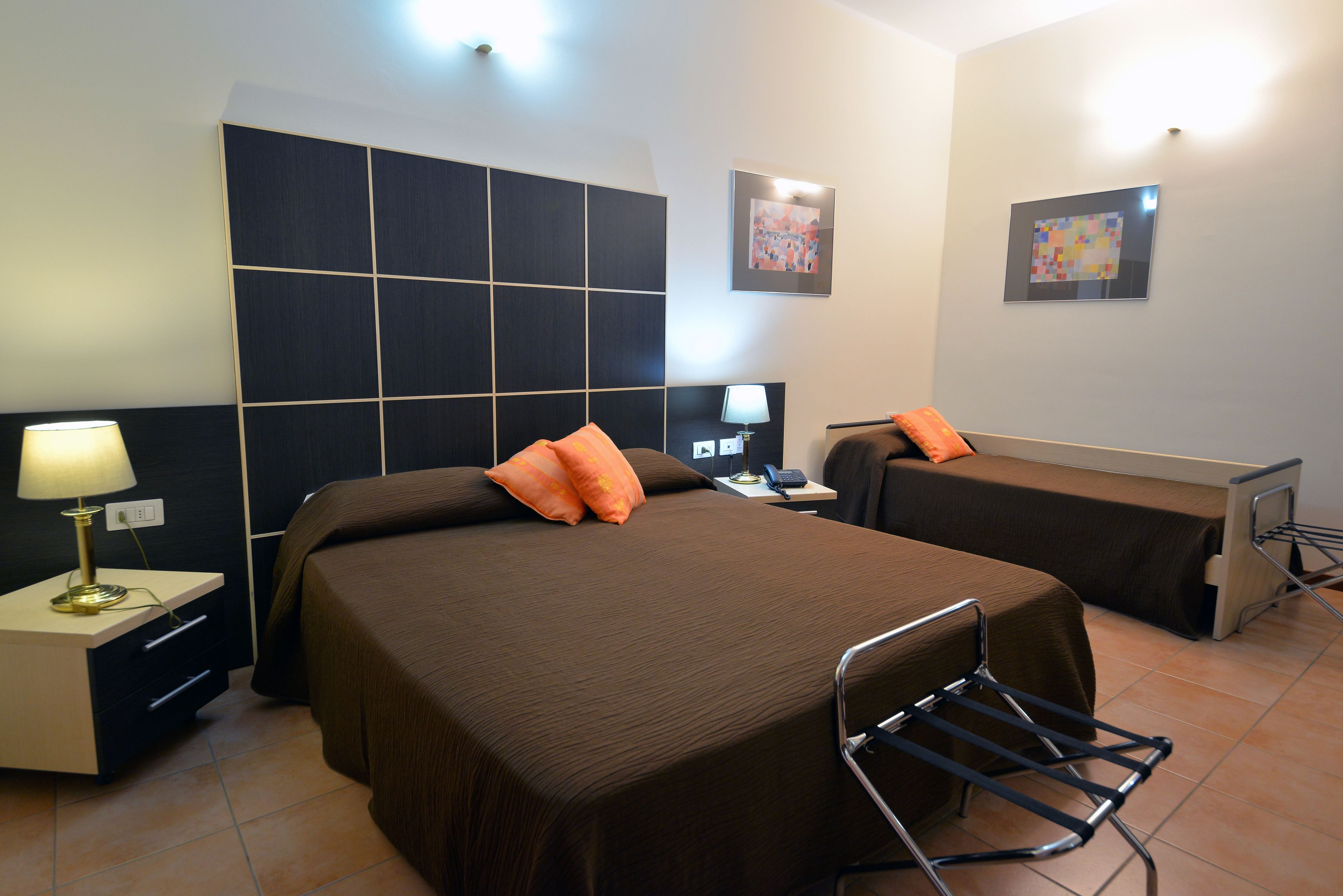 Een hotelkamer met een groot bed, een kleiner bed, een bureau met een lamp en een stoel.
