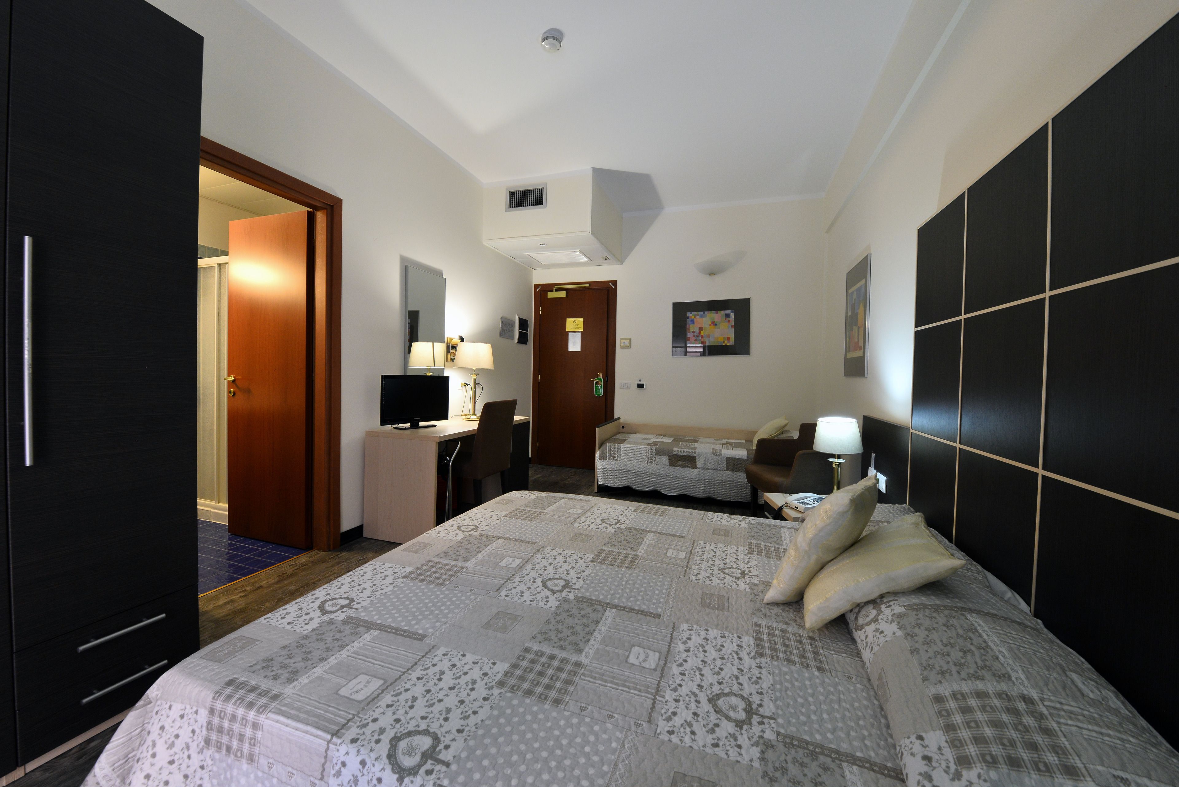 A hotel room with a bed, a desk, a chair, a TV, and a wardrobe.