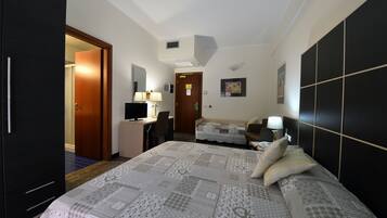A hotel room with a bed, a desk, a chair, a TV, and a wardrobe.