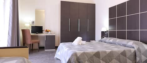 A hotel room with a bed, a desk with a computer, a chair, and a wardrobe.