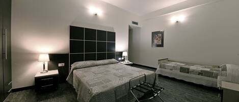 Una habitación de hotel moderna con una cama grande, una cama adicional, una mesita de noche con una lámpara, un televisor montado en la pared y un armario.