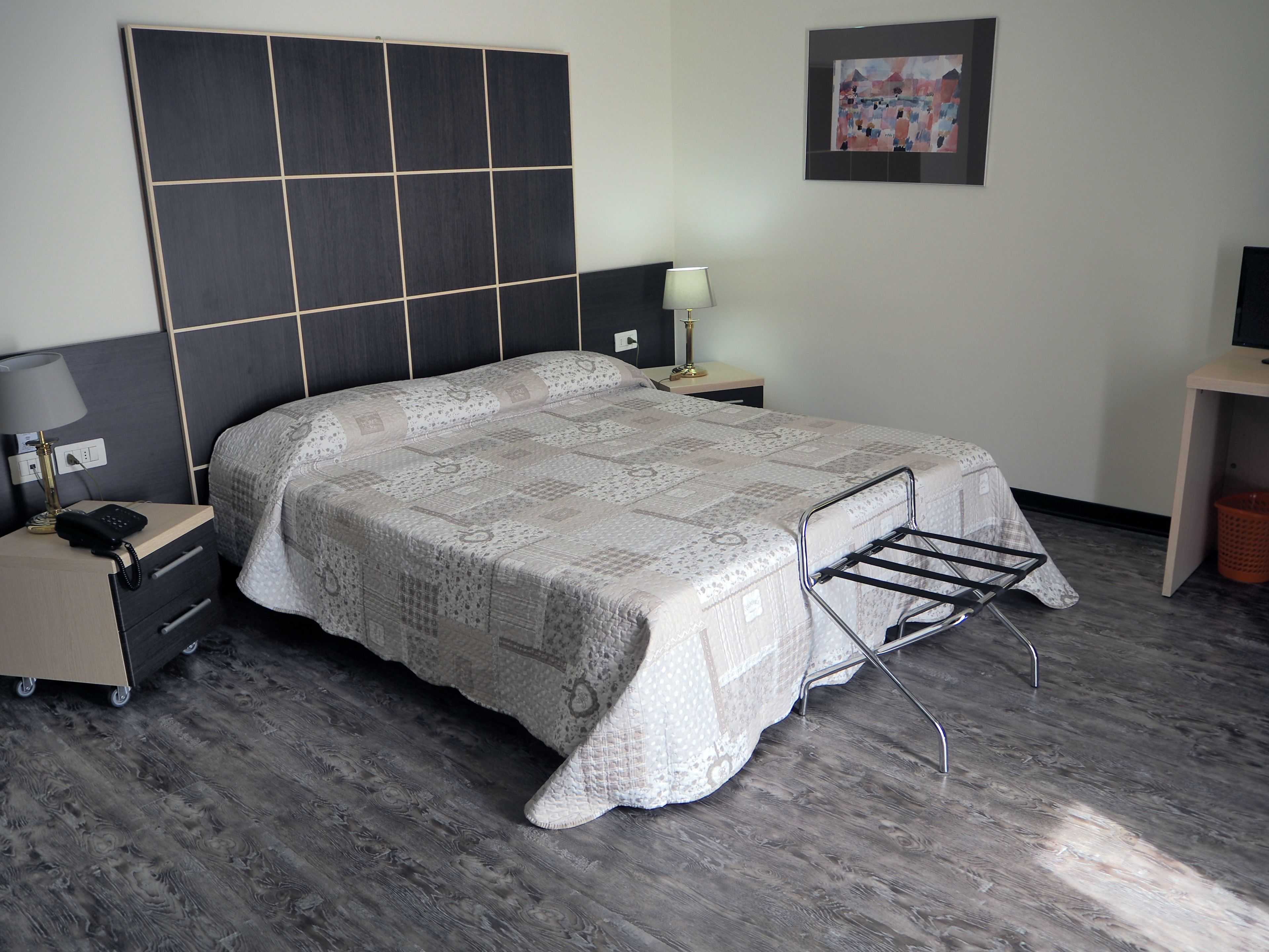 Una camera da letto con un letto grande, un comodino con una lampada, un mobile TV e un’opera d’arte appesa al muro.