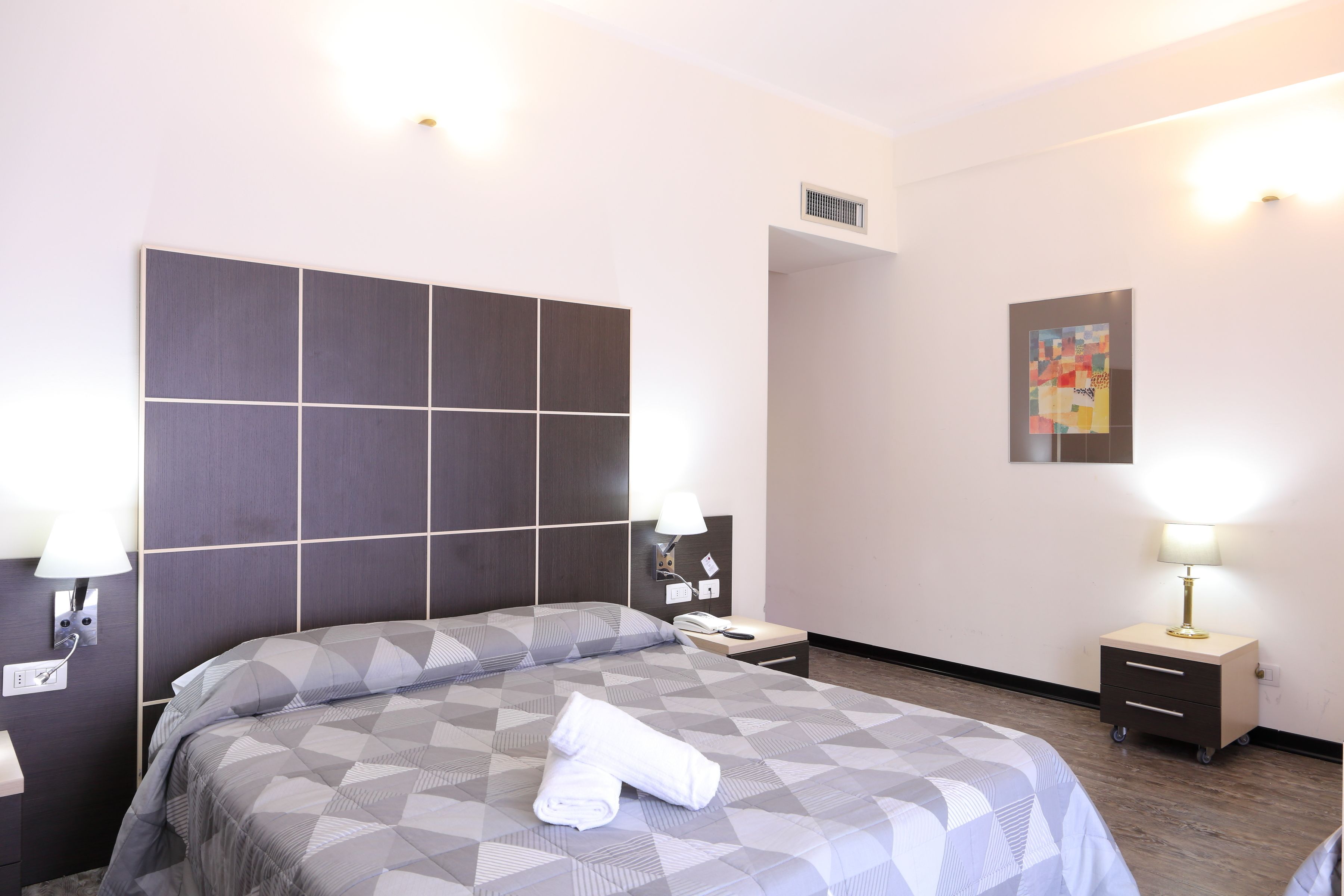 Une chambre d’hôtel avec un grand lit, une table de chevet avec une lampe, une petite table et une œuvre d’art accrochée au mur.