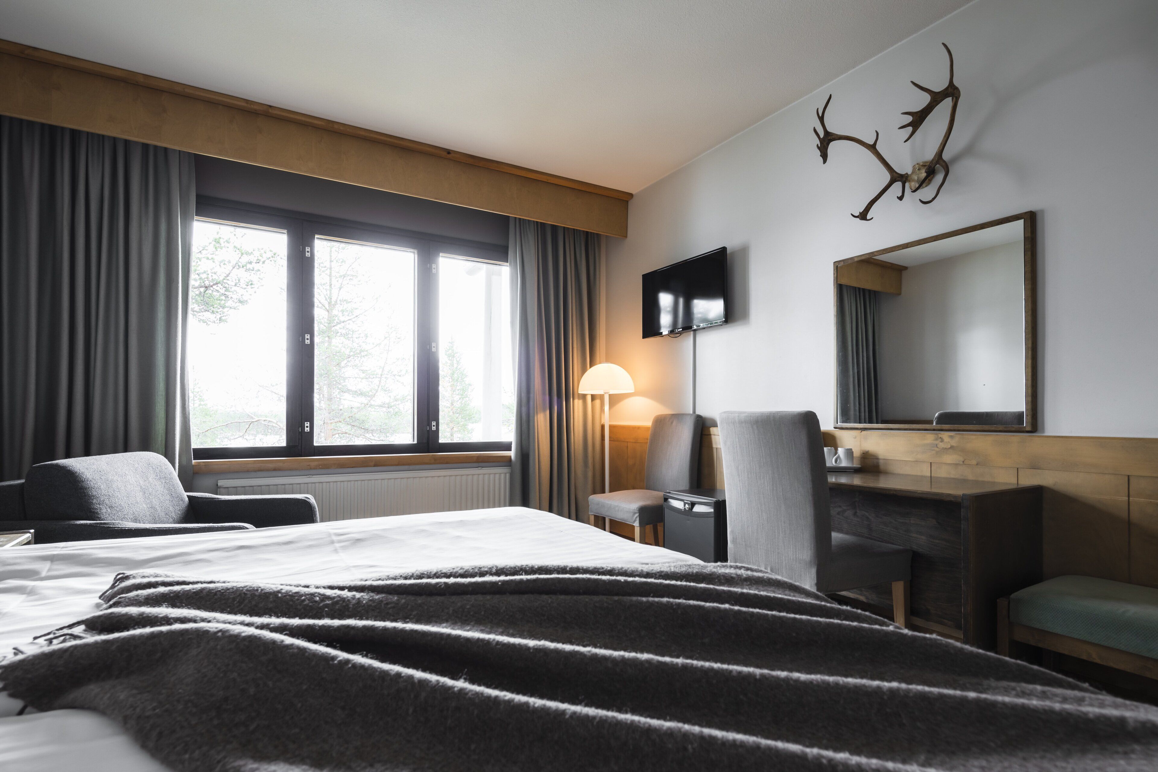 A hotel room with a large bed, a desk, a chair, a TV, and a window with curtains.