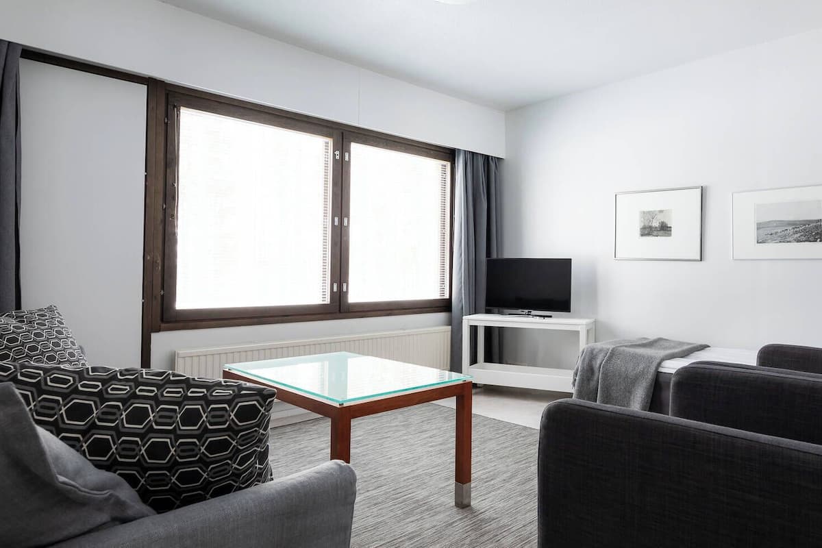 A modern living room with a glass-top coffee table, grey sofas, a flat-screen TV on a white stand, and two framed pictures on the wall.