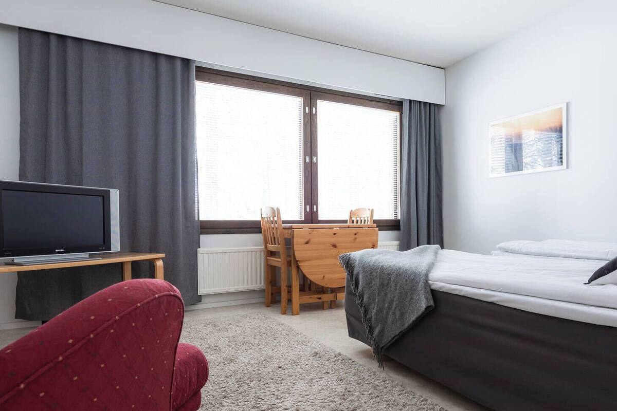 A hotel room with a bed, a TV, a dining table, and a chair.