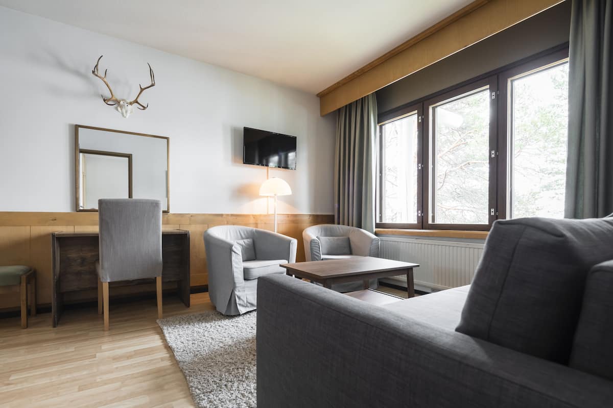 A modern living room with a sofa, two armchairs, a coffee table, a TV, and a mounted deer skull.