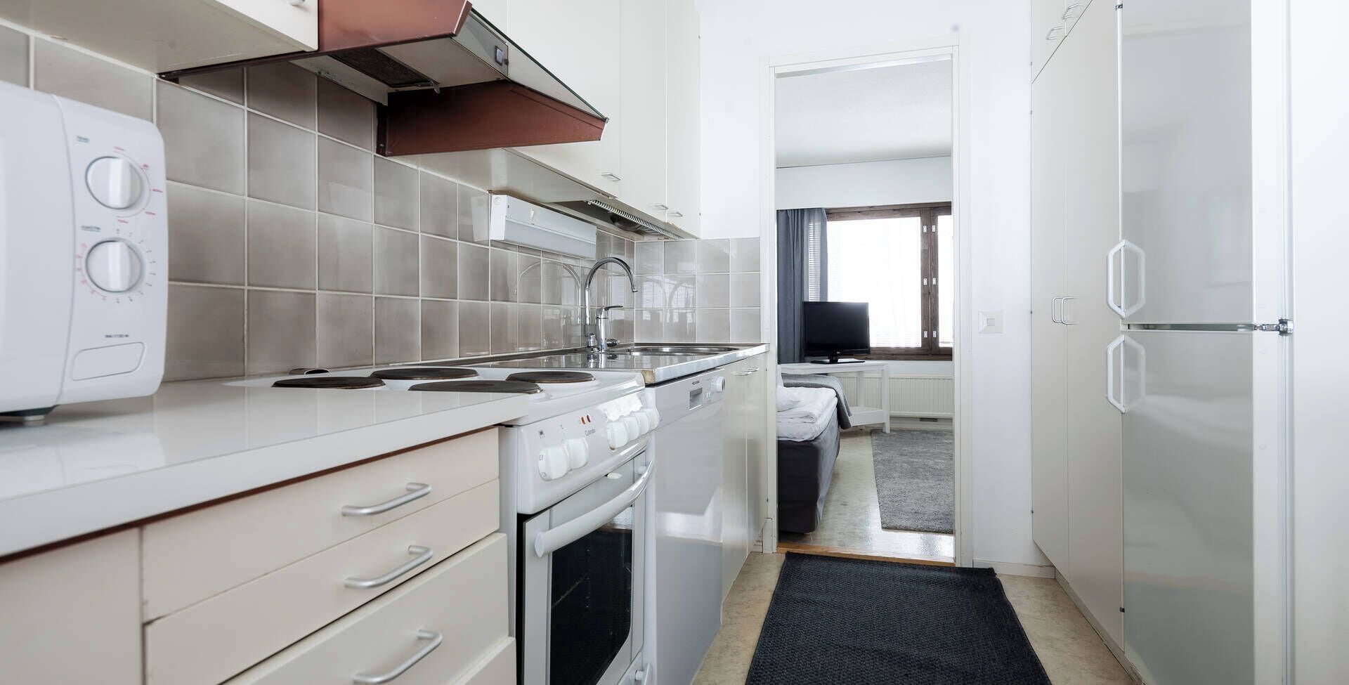 Cocina compacta con estufa, horno y microondas, un lavamanos pequeño y una ventana con vistas.