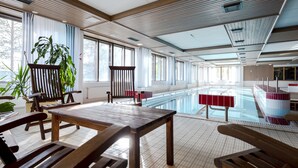 A spacious indoor swimming pool area with wooden benches and a table, large windows, and a view of the outside. - Lapland Hotels Hetta (Enontekio)