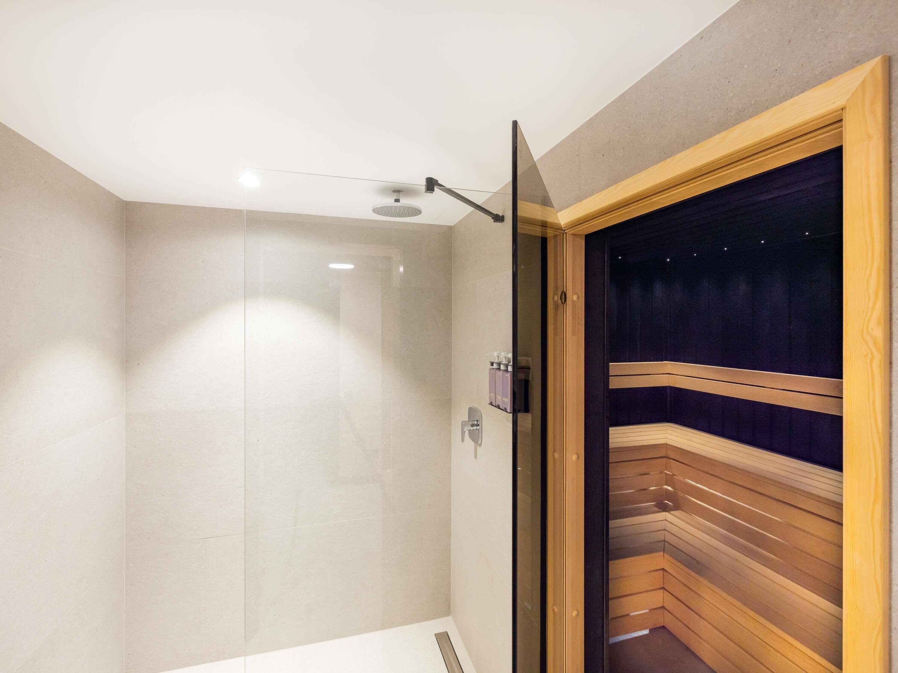 A modern bathroom with a glass shower enclosure, a wooden bench, and a dark-colored wall.