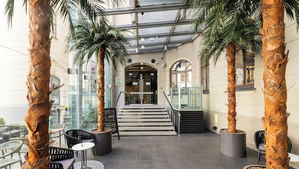 A modern indoor area with palm trees, a staircase, and seating arrangements. - TRIBE Riga City Centre Hotel - Renovated 2026 (Riga)