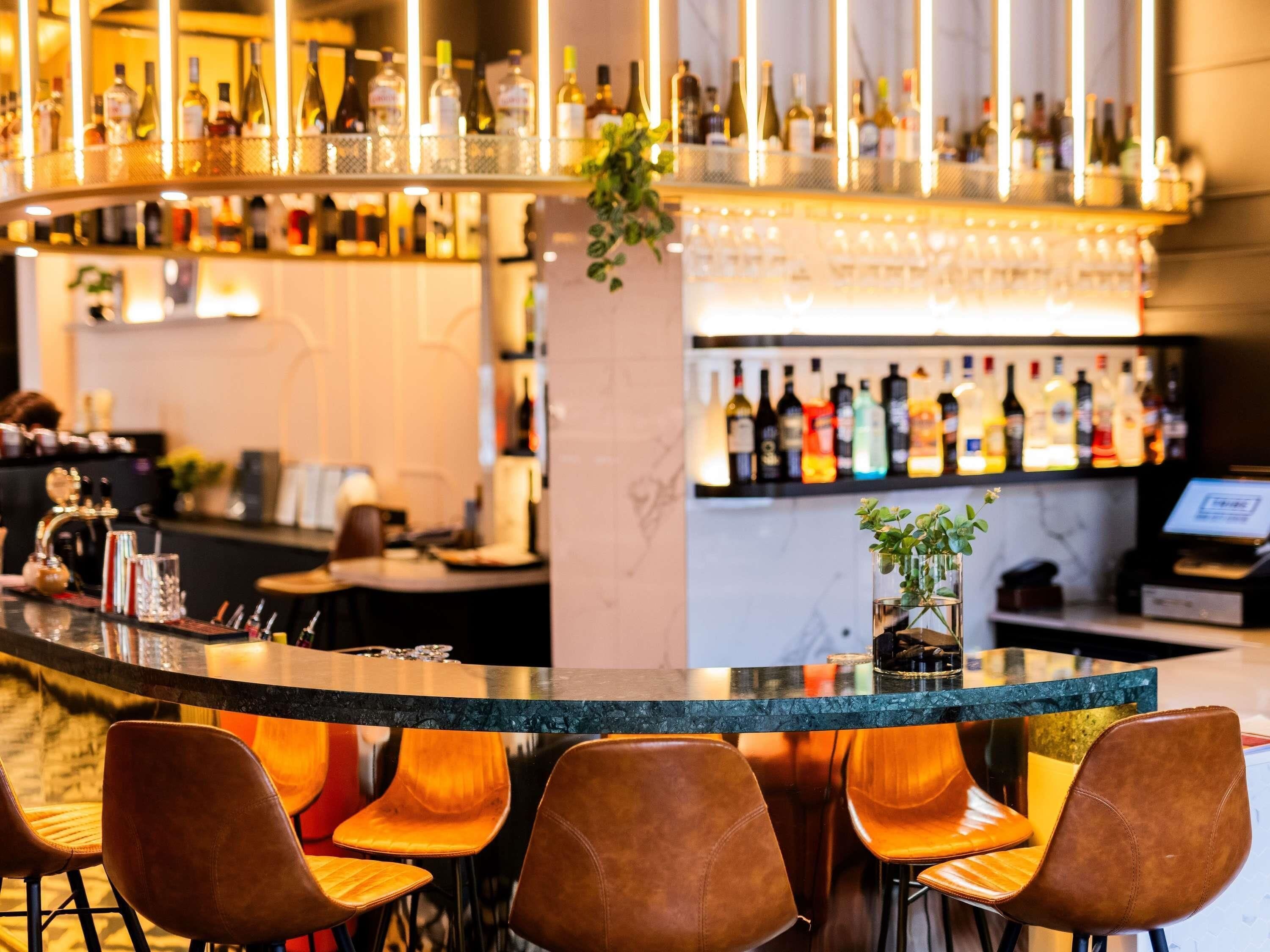 A bar area with a curved counter, multiple seating options, and a variety of bottles on shelves.