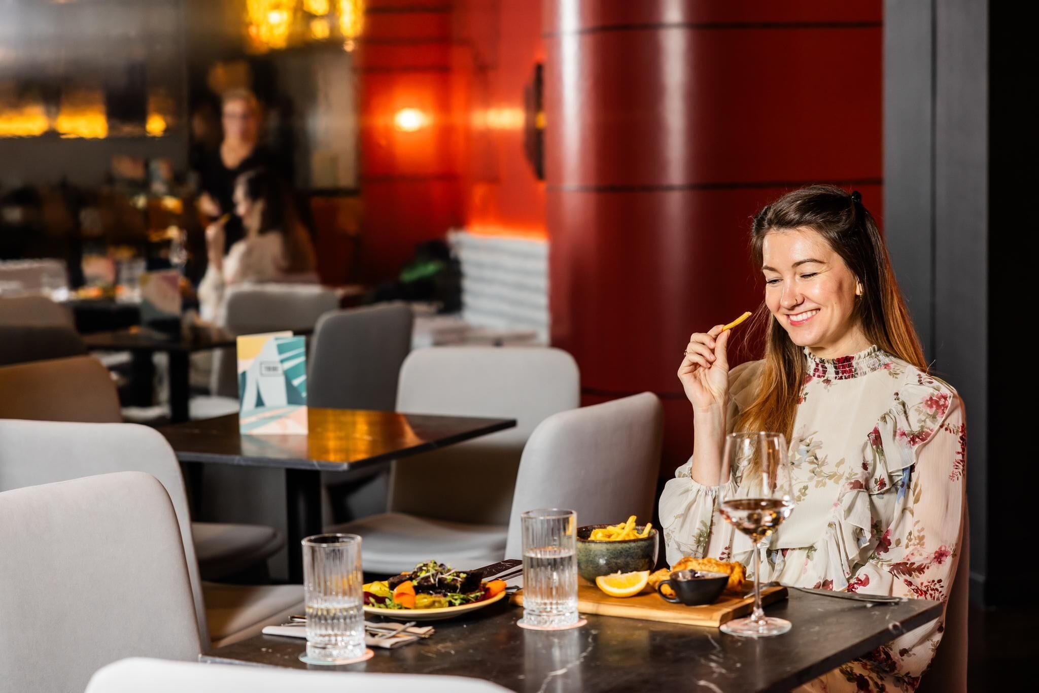 Una persona comiendo en un restaurante, con una mesa servida con platos, vasos y un bol de comida.