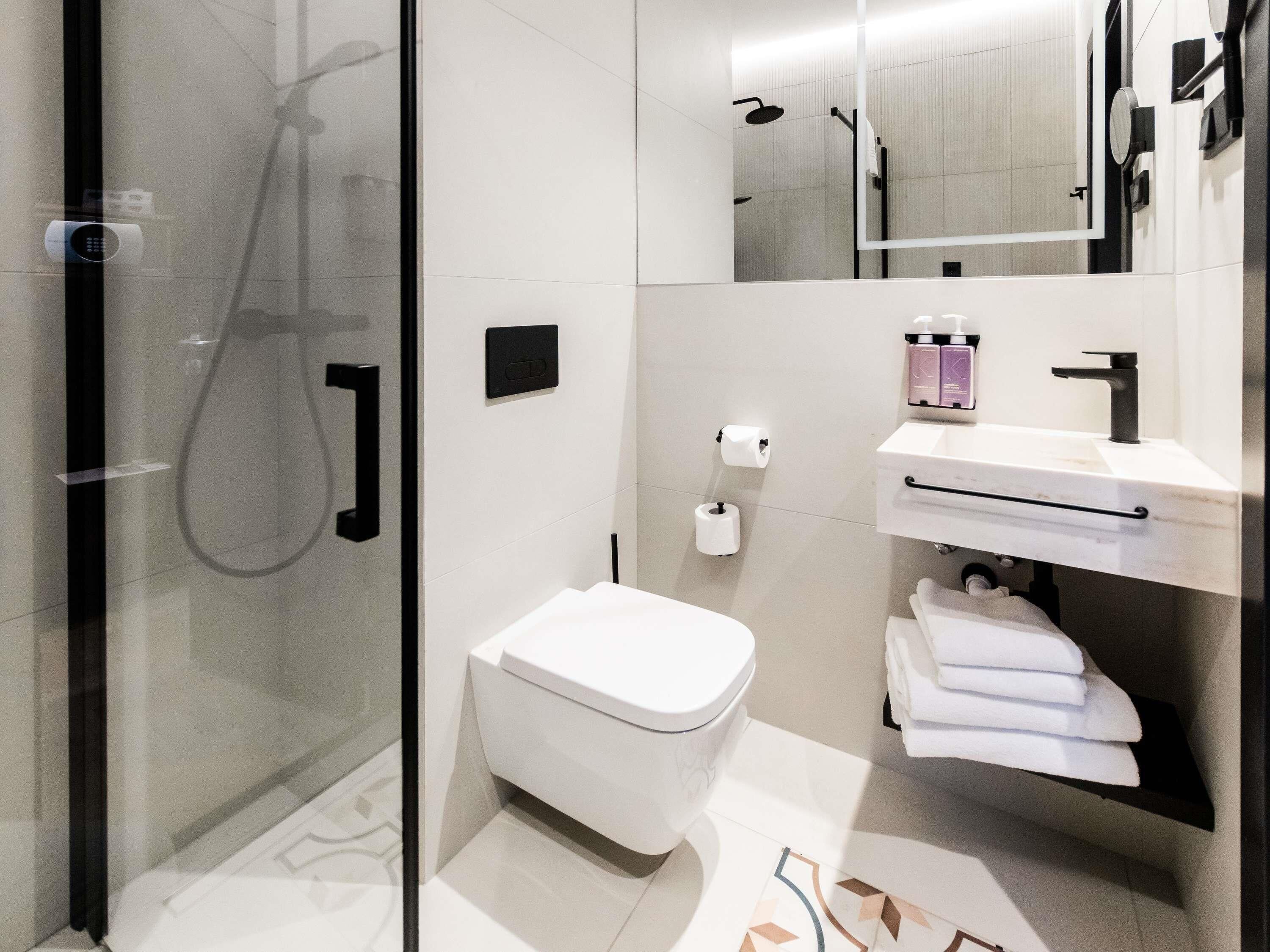 Un baño moderno con cabina de ducha de vidrio, inodoro blanco, lavabo con espejo y toallero.