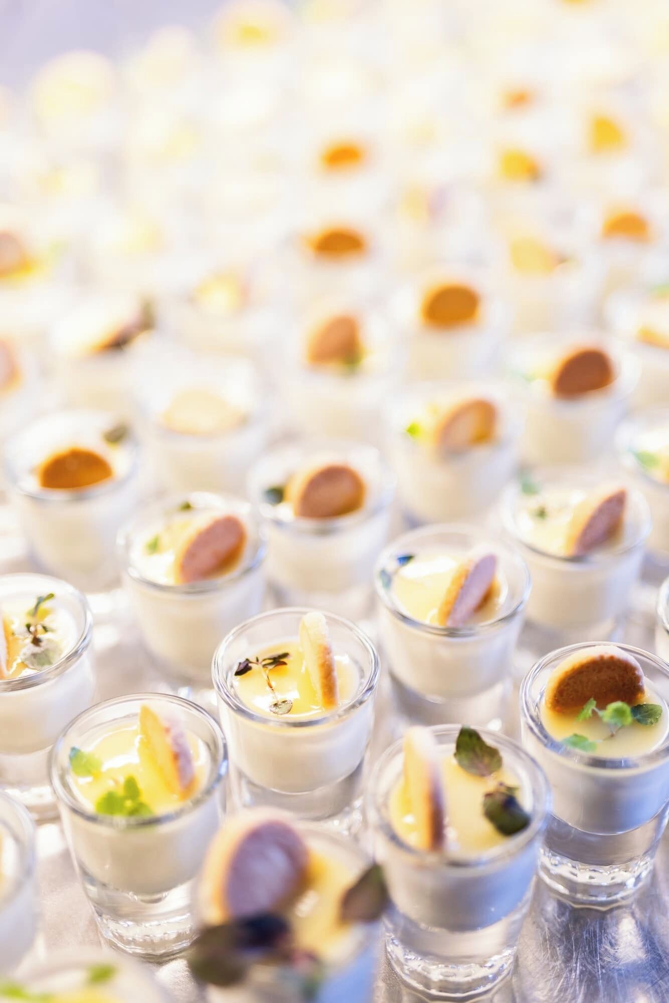 A series of clear glass shot glasses filled with a creamy dessert, garnished with a slice of fruit and a dollop of sauce.
