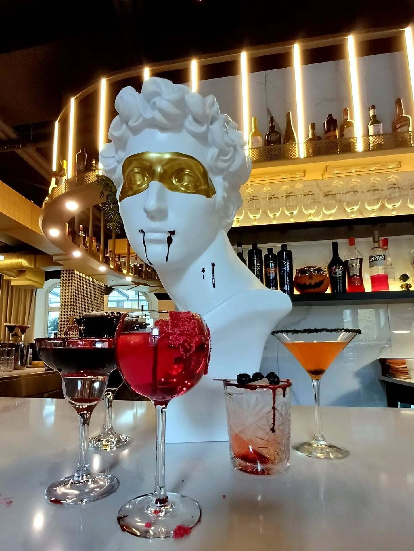 A bar area with a white bust sculpture, various bottles, and three different drinks on the counter.