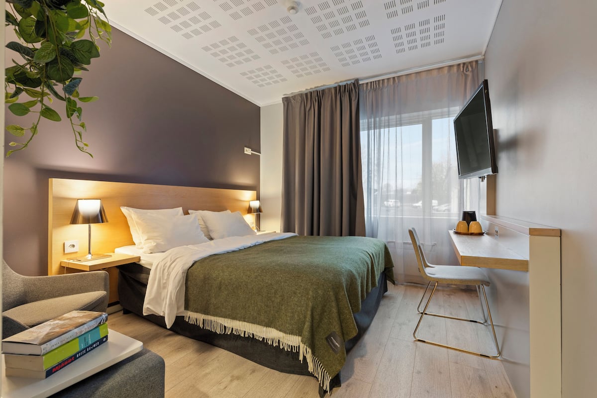 A modern hotel room with a bed, bedside table, lamp, and a TV mounted on the wall.