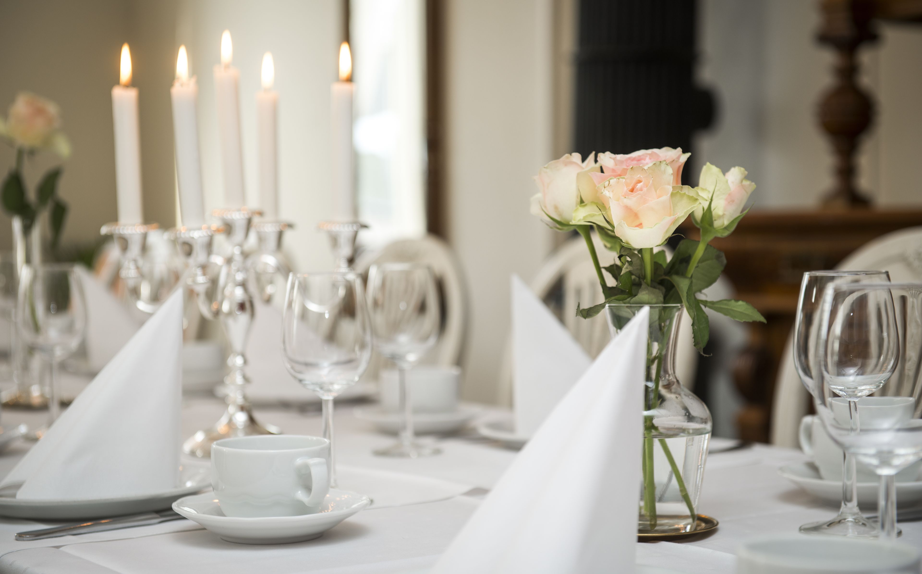 A formal dining table set with white tableware, clear glassware, and a vase with a single rose.