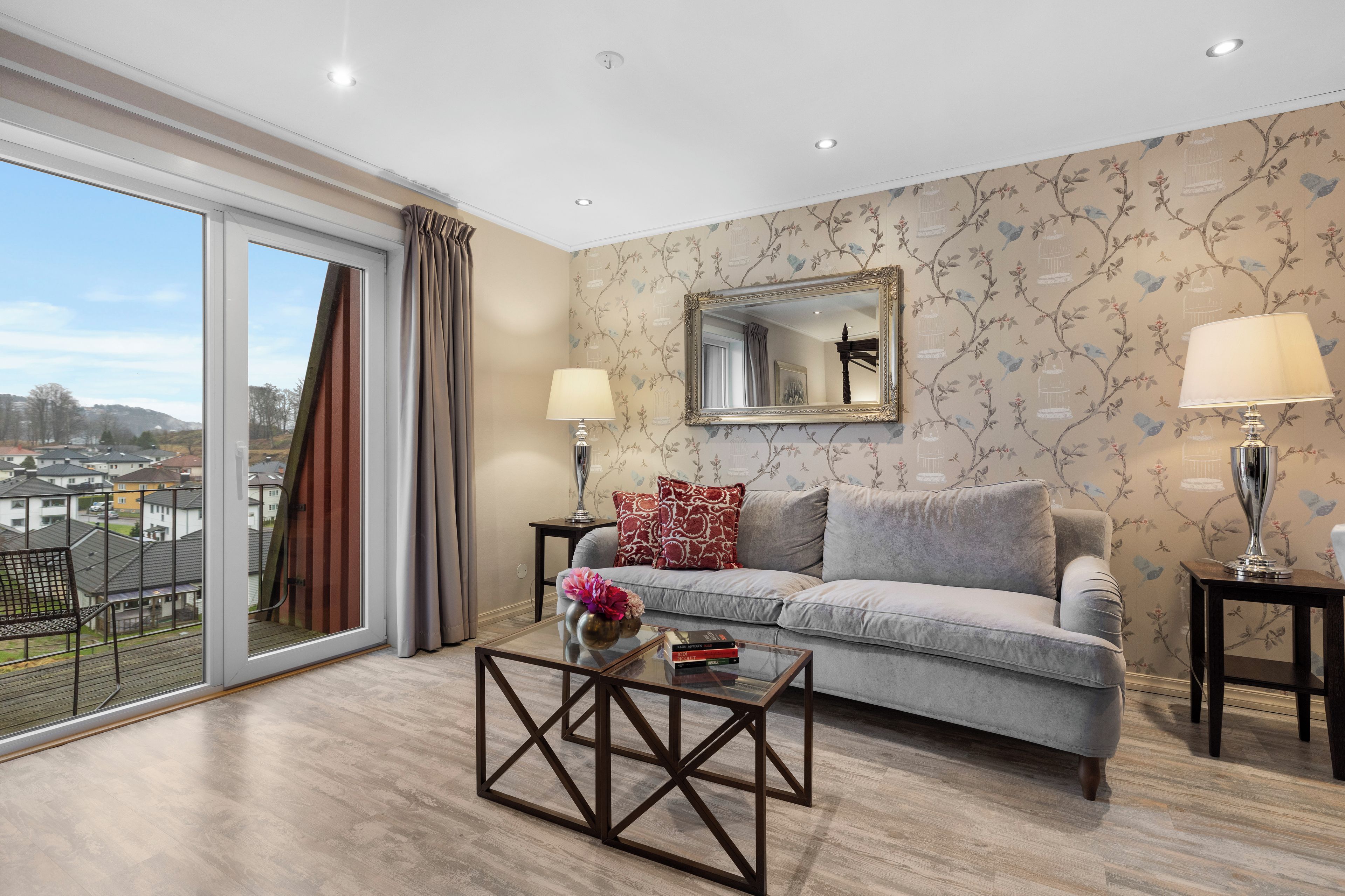 Una sala de estar moderna con un sofá gris, una mesa de centro de vidrio y un ventanal con cortinas.