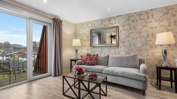 A modern living room with a grey sofa, a glass coffee table, and a large window with curtains.