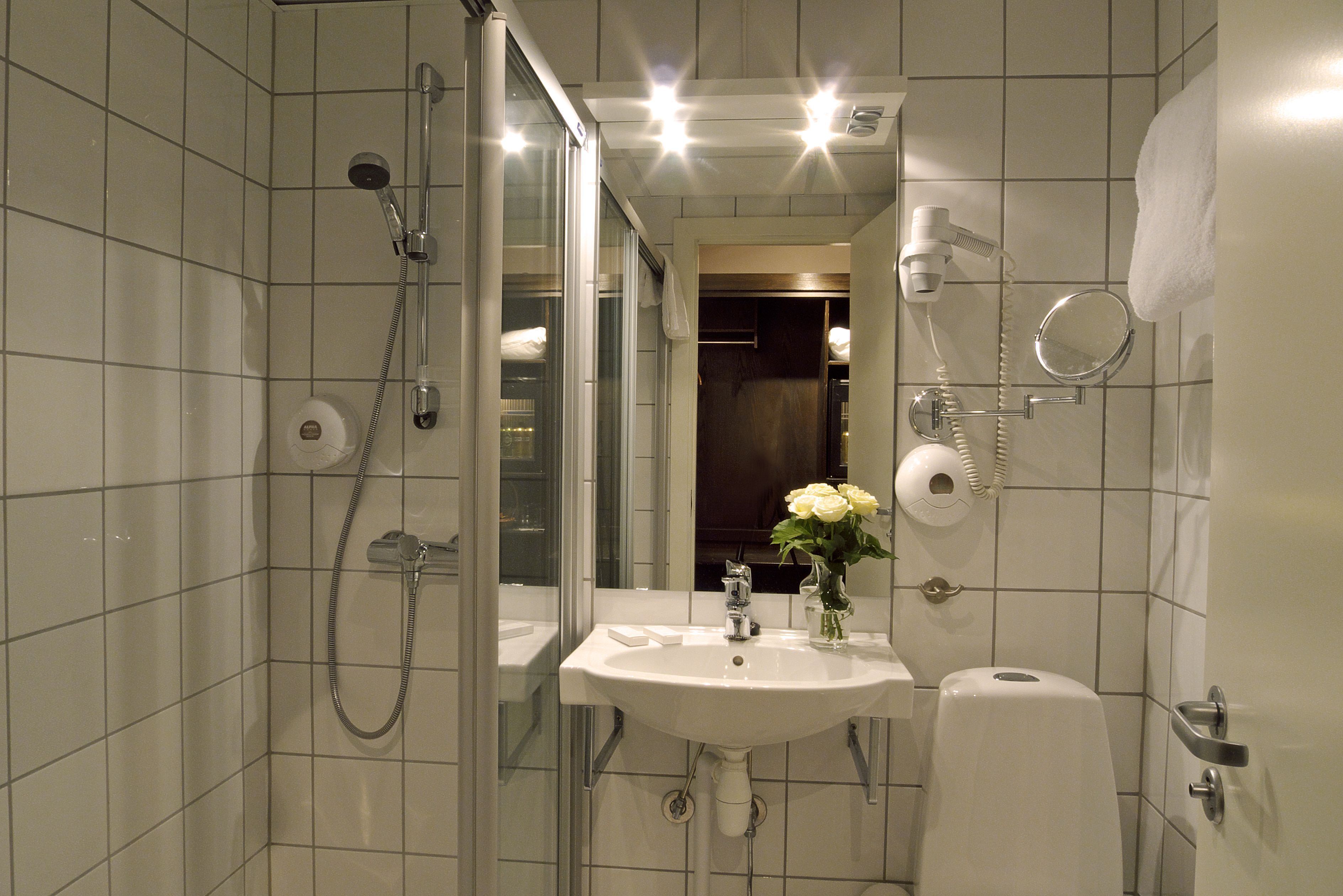 A modern bathroom with a glass-enclosed shower, a sink with a vase of flowers, and a towel hanging on the wall.