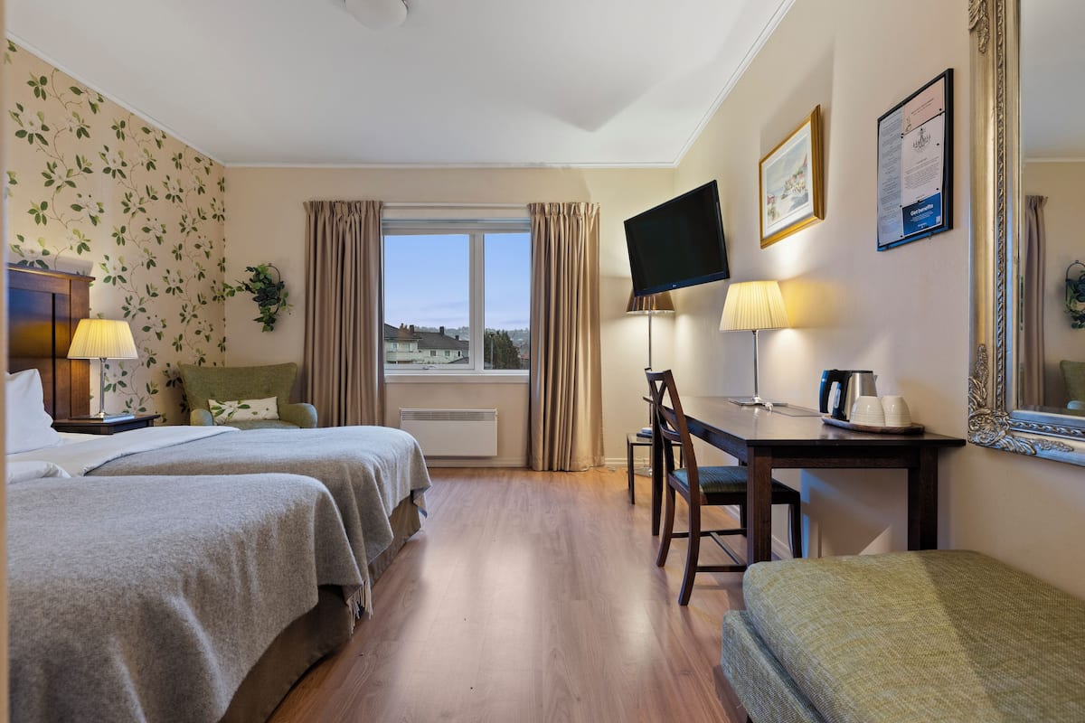 A hotel room with two beds, a desk with a chair, a TV, and a window with curtains.