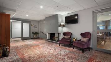 Eine moderne Lobby mit Teppichmuster, zwei Sesseln, einem Kamin und einem an der Wand befestigten Flachbildfernseher.