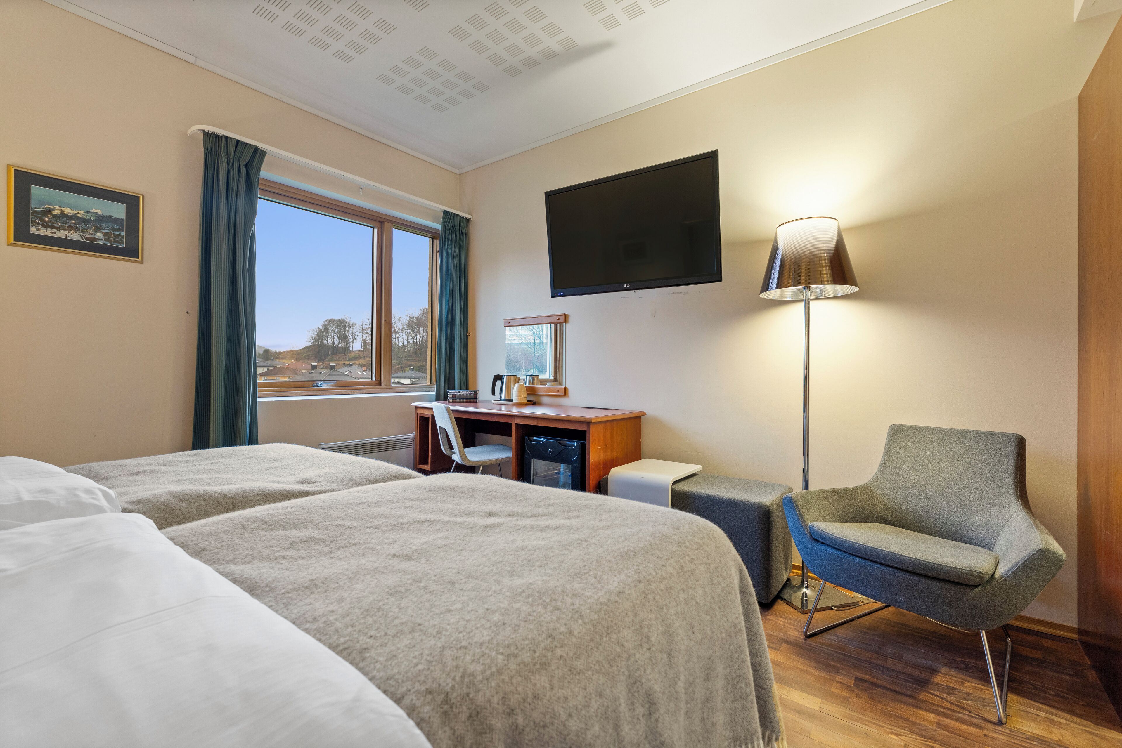 Hotelkamer met twee bedden, een bureau, een stoel, een televisie en een raam met gordijnen.
