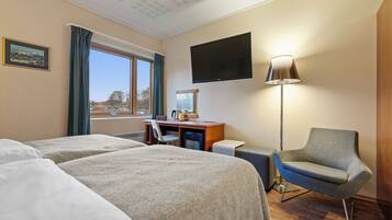 Hotelkamer met twee bedden, een bureau, een stoel, een televisie en een raam met gordijnen.