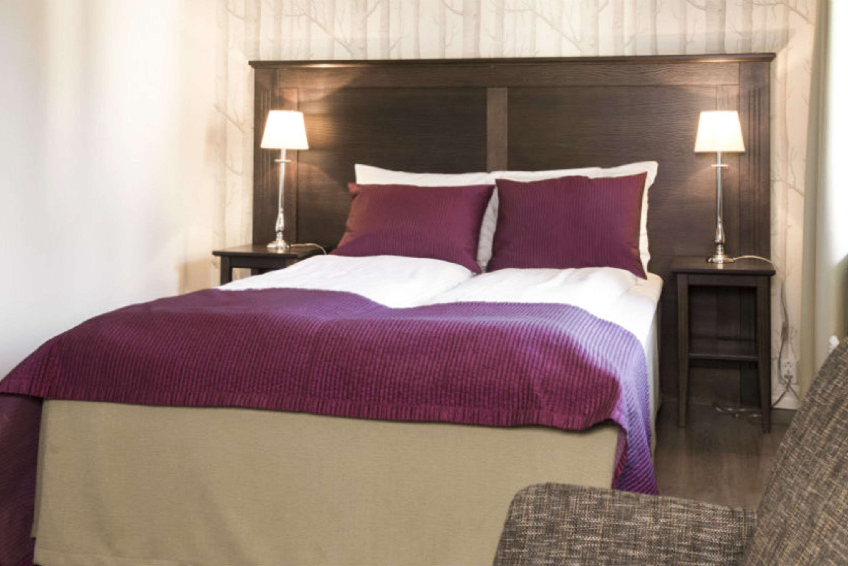 A hotel room with a large bed, two bedside tables with lamps, and a chair.