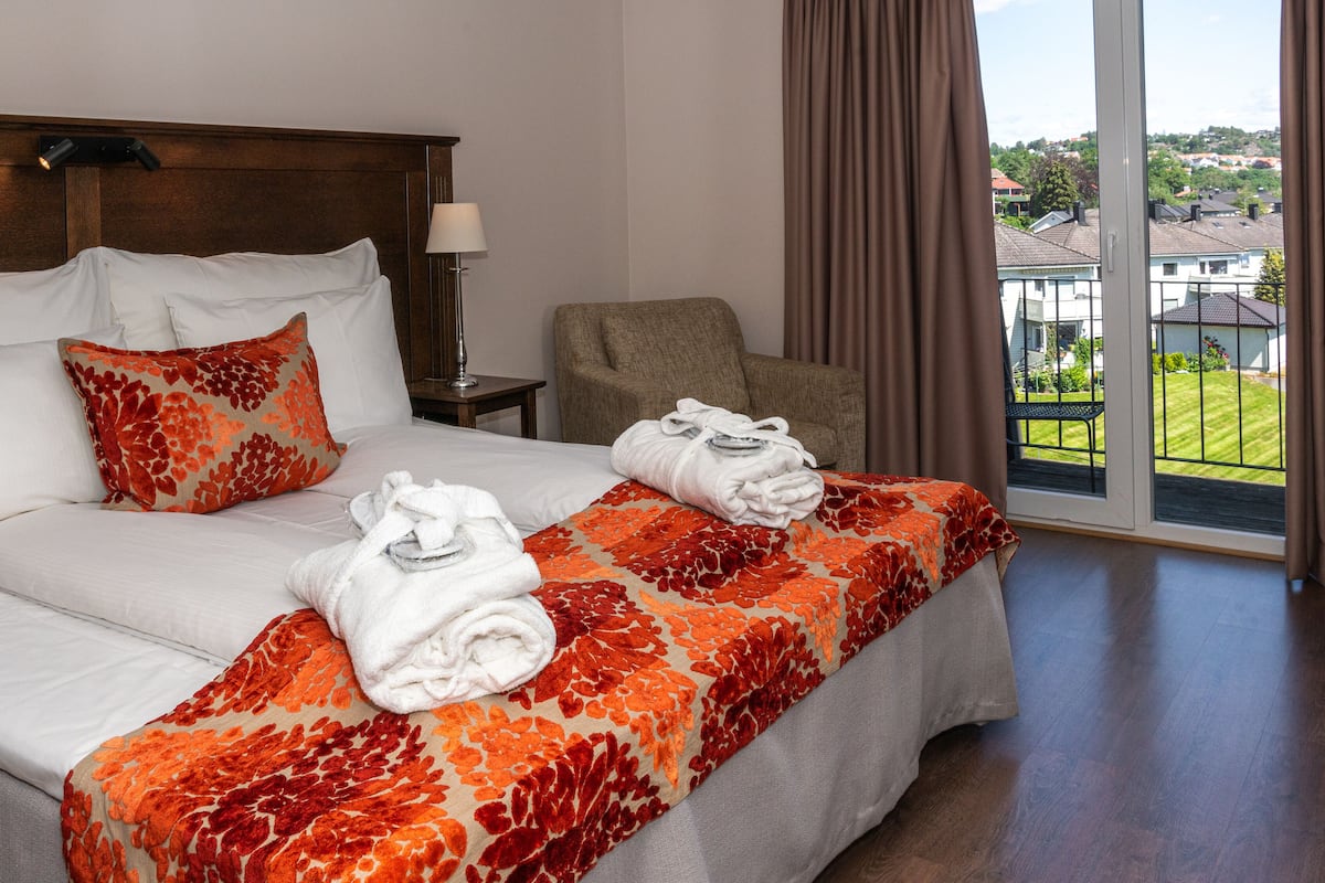 A hotel room with a large bed, two pillows, a nightstand, a chair, and a view of the outside.