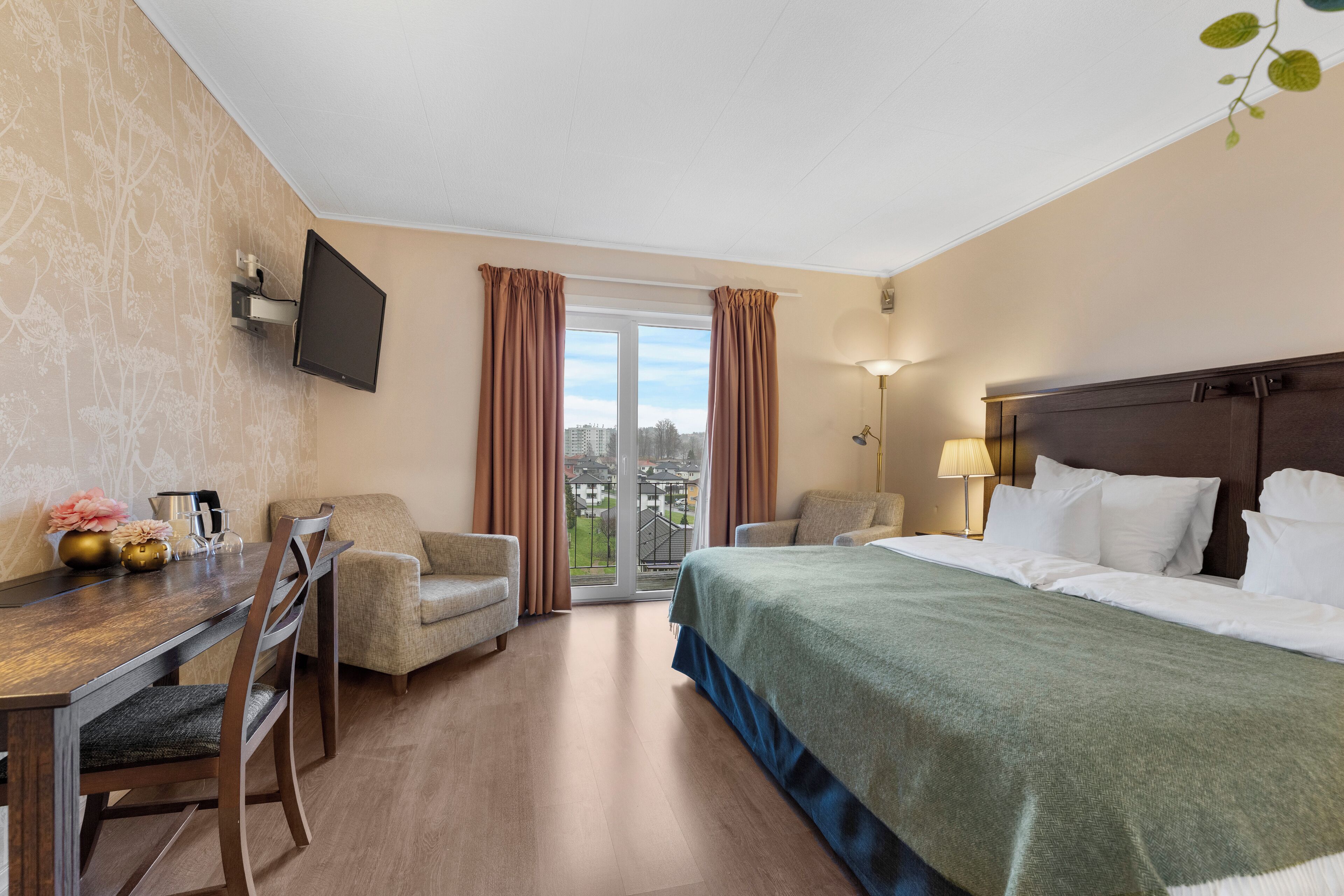 Une chambre d’hôtel avec un lit, un bureau, deux chaises, un téléviseur fixé au mur et une vue sur la ville par la fenêtre.