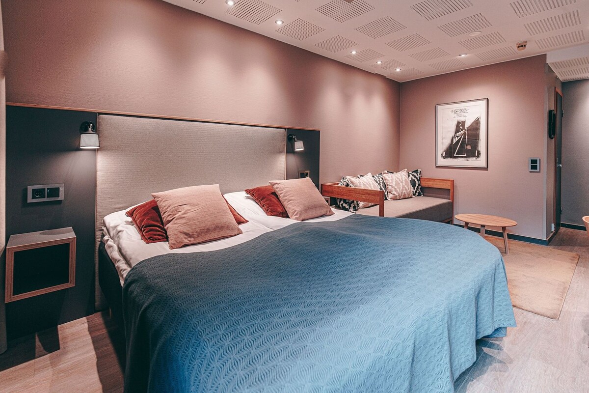 A modern bedroom with a large bed, bedside tables, a nightstand, and a wall-mounted light fixture.
