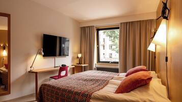 Une chambre d’hôtel comprenant un lit, un bureau avec une chaise, un téléviseur fixé au mur et une fenêtre avec des rideaux.