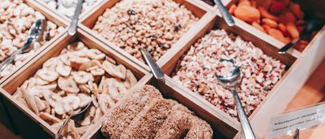 Diversos alimentos em caixas de madeira, incluindo nozes, frutas secas e granola, com colheres.