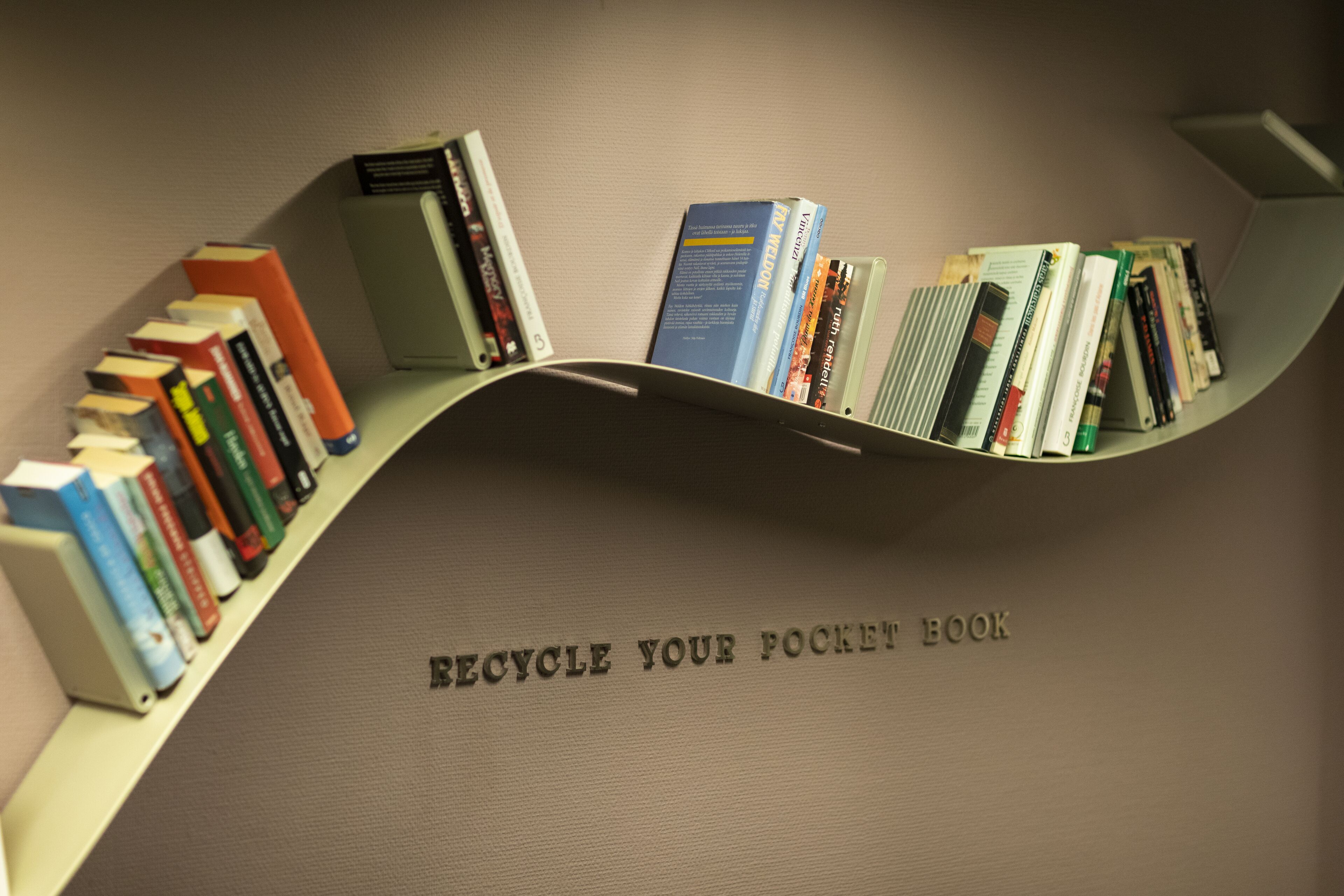A curved bookshelf with books and a sign that reads "RECYCLE YOUR POCKET BOOK".