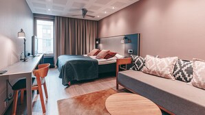 Une chambre d’hôtel moderne équipée d’un lit, d’un canapé, d’un bureau, d’une chaise et d’une table ronde.