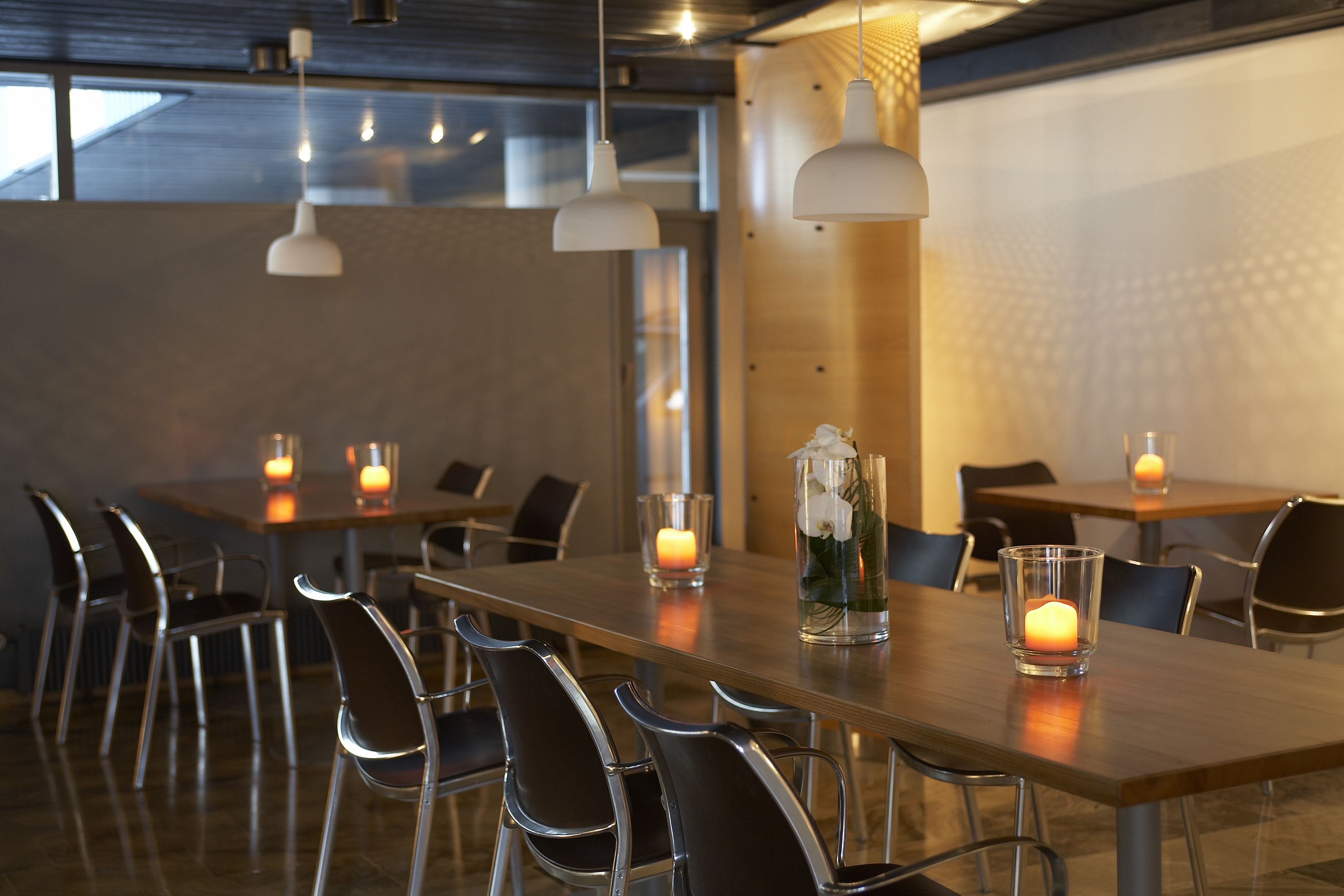Een moderne eetruimte met houten tafels en metalen stoelen, met hanglampen en kaarsen.