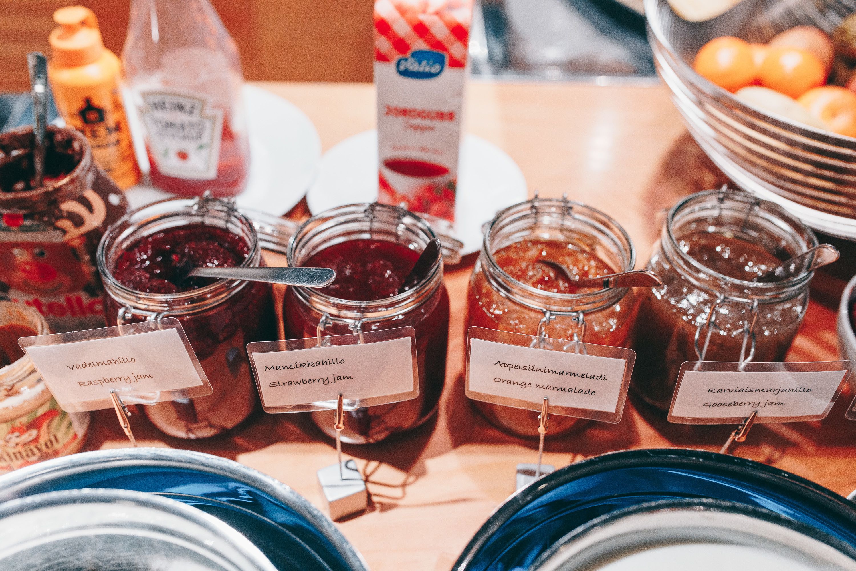 A variety of jars labeled with different types of jams, including raspberry, strawberry, orange marmalade, and gooseberry jam.