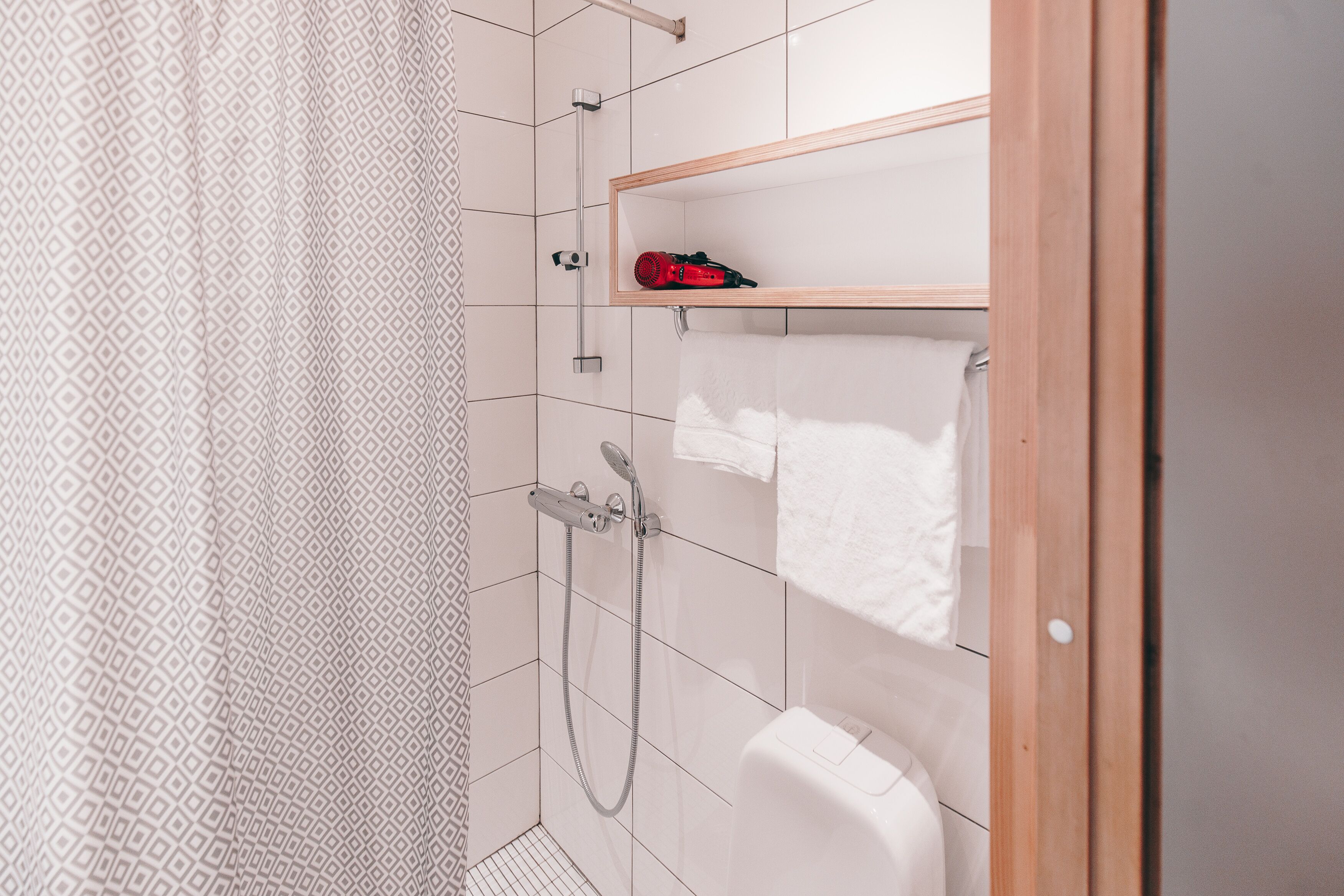 A bathroom with a shower, a toilet, and a shelf with a towel.